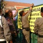 Petugas dari Sapol PP melakukan penutupan dengan memasang papan pengumuman. Foto: khumaidi/BANGSAONLINE