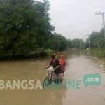 TETAP SETIA: Sepasang kekasih harus menuntun sepedanya untuk melewati banjir. foto: eki nurhadi/ BANGSAONLINE