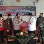 Plt Bupati Nganjuk Marhaen Jumadi menerima potongan tumpeng dari Kapolres Nganjuk AKBP Harviandhi saat peresmian Desa Tanjungrejo sebagai Kampung Tangguh Bersih Narkoba. foto: BAMBANG/ BANGSAONLINE