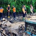 Petugas BPBD Blitar membersihkan puing-puing yang terbawa arus saat banjir bandang terjadi.