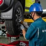 Kendaraan Suzuki yang sedang diperiksa ban belakangnya oleh montir.