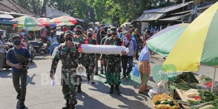 Anggota TNI dan Polri membopong pocong sambil menyosialiasasikan bahaya Covid-19 di Pasar Legi Jombang. foto: AAN AMRULLOH/ BANGSAONLINE