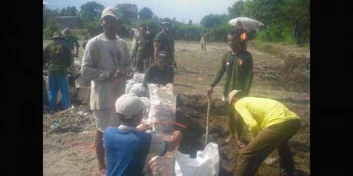 Warga dan pasukan TNI membuat tanggul buatan dari karung yang disi pasir dan kerikil.