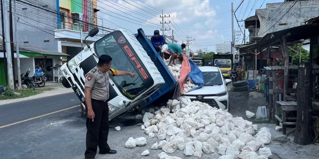 Truk muatan batu kapur yang terguling hingga menimpa sebuah mobil yang sedang terparkir