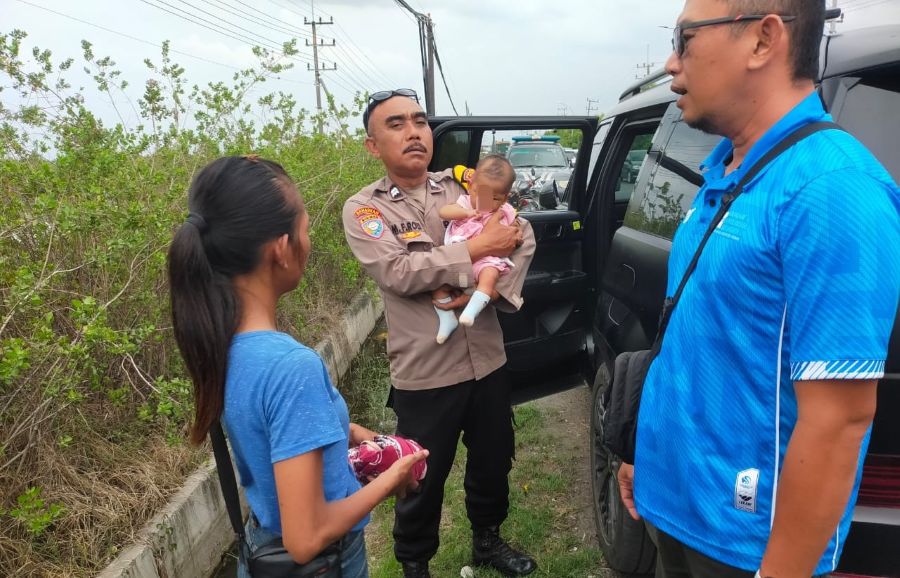 Petugas menggendong bayi pasangan suami istri berprofesi pengamen yang diletakkan di tepi jalan usai terlibat cekcok. Foto: Ist.