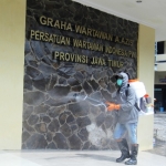 Salah seorang petugas menyemprotkan disinfektan di depan Kantor PWI Jatim, Jumat (27/3/2020).  