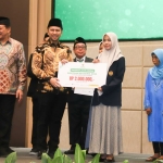 Ketua Baznas Jatim KH Ali Maschan Moesa saat menyerahkan beasiswa program SKSS kepada seorang siswi saat rakorda. Foto: YUDI A/BANGSAONLINE