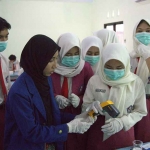 Para siswa dibantu oleh mahasiswa sedang mengukur suhu metanol yang telah dipanaskan menggunakan thermogun pada saat sesi praktikum.