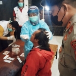Seorang petugas Sabhara Polres Ngawi menyaksikan salah satu pengunjung kafe sedang dites PCR oleh tim medis.