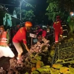 Sejumlah petugas gabungan beserta warga saat bekerja sama mengevakuasi material pagar tembok yang ambrol saat hujan deras di Kota Malang.
