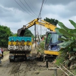 Alat berat saat mengangkut sisa material banjir ke sebuah truk. Foto: MUJI HARJITA/ BANGSAONLINE