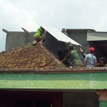 Warga dibantu petugas dari TNI yang sedang membetulkan atap asbes yang melorot.