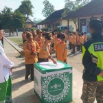
Siswa MI Al Falah Desa Pagu, Kecamatan Wates, Kabupaten Kediri saat antri memasukkan koin ke kotak koin NU. (Ist).