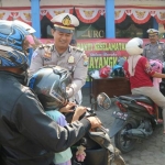 Kanit Laka Lantas Polres Bangkalan Iptu Didit saat memasangkan helm kepada pengendara R2 yang tidak menggunakan helm di Pos Lantas Halim, Selasa (2/7). foto: ist