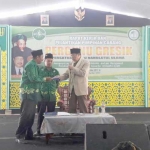 Mantan Menag RI KH. Tolchah Hasan saat memberikan buku kepada Ketua PC Pergunu Gresik Ach. Sururi. foto: SYUHUD/ BANGSAONLINE