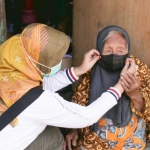 Petugas dari Dinsos Kota Kediri saat memakaikan masker untuk menutupi hidung Mbah Sri Wartini. foto: ist.