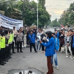 Ketua PMII Kediri Saiful Amin saat membacakan tuntutan mahasiswa dalam aksi demo yang dijaga ketat oleh aparat kepolisian dari Polres Kediri. Foto: MUJI KEDIRI/ BANGSAONLINE