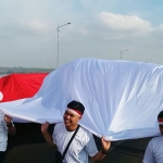 Masyarakat dan Polres Bangkalan bersama-sama membentangkan bendera merah putih sepanjang 3.000 meter di Jembatan Suramadu. foto: FAUZI/ BANGSAONLINE