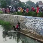 Pengendara motor yang nyungsep ke sungai saat ditolong oleh warga setempat.