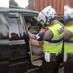 Petugas kepolisian saat mengevakuasi seorang pria yang meninggal dalam mobil akibat serangan jantung di Jalan Raya Geluran, Sidoarjo.