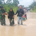 Personel Koramil 0817/09 Balongpanggang menuntun ibu-ibu melintas di jalan kebanjiran di Desa Wotansari, dampak luapan Kali Lamong. foto: ist.
