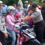 Anggota Polsek Simokerto membagikan helm kepada anak-anak. (ft: rusmiyanto/BANGSAONLINE)
