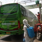 Bus yang akan mengangkut para santri pulang ke daerahnya masing-masing, sedang disemprot dengan cairan disinfektan ketika memasuki pintu gerbang Ponpes Lirboyo. (foto: ist)