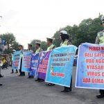 Anggota Satlantas Polres Jombang membentangkan poster berisi ajakan kepada masyarakat agar tak keluar rumah untuk sementara waktu. foto: AAN AMRULLOH/ BANGSAONLINE