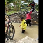 Para pegowes harus turun dan menerobos aliran sungai sambil menggotong sepedanya setelah jembatan penghubung Desa Munggugebang - Sirnoboyo, Benjeng putus diterjang arus Kali Lamong. foto: ist.