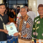 Kasubag TU Kantah Pasuruan, Totok Mashudianto, saat menyerahkan sertifikat tanah program PTSL secara simbolis kepada salah satu warga Desa Ngadimulyo. Foto: Ist.