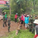 Anggota TNI-AD dan warga desa gotong royong memperbaiki jembatan.
