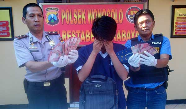 Tersangka diapit Kapolsek dan Kanit Reskrim memegang uang hasil penggelapan. (rusmiyanto/BANGSAONLINE)