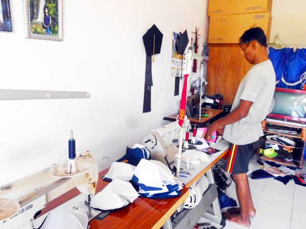 ?Joko saat mengerjakan pesanan topi SMP. Tampak juga topi wisuda dan dasi SD. foto: rizky alvian/BANGSAONLINE