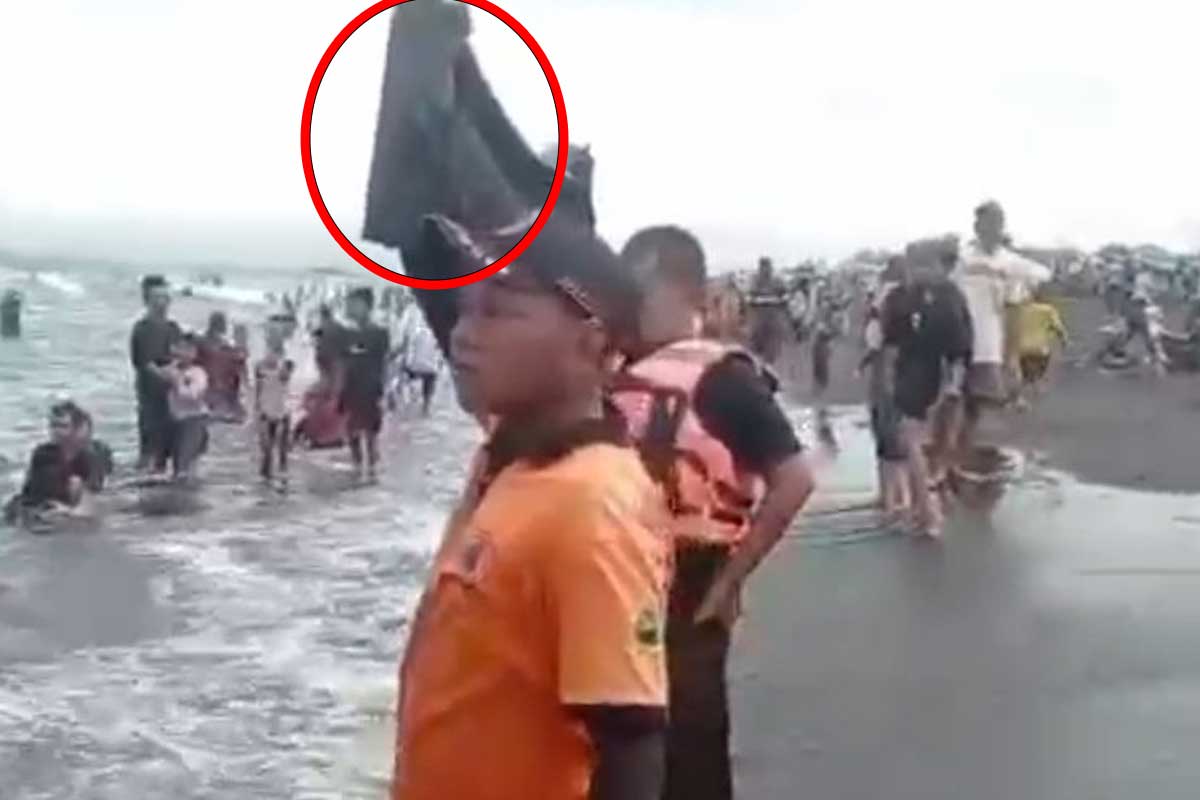 Salah satu relawan dari BPBD Jember, peringatkan wisatawan yang mandi di Pantai Paseban dengan kantong jenazah.