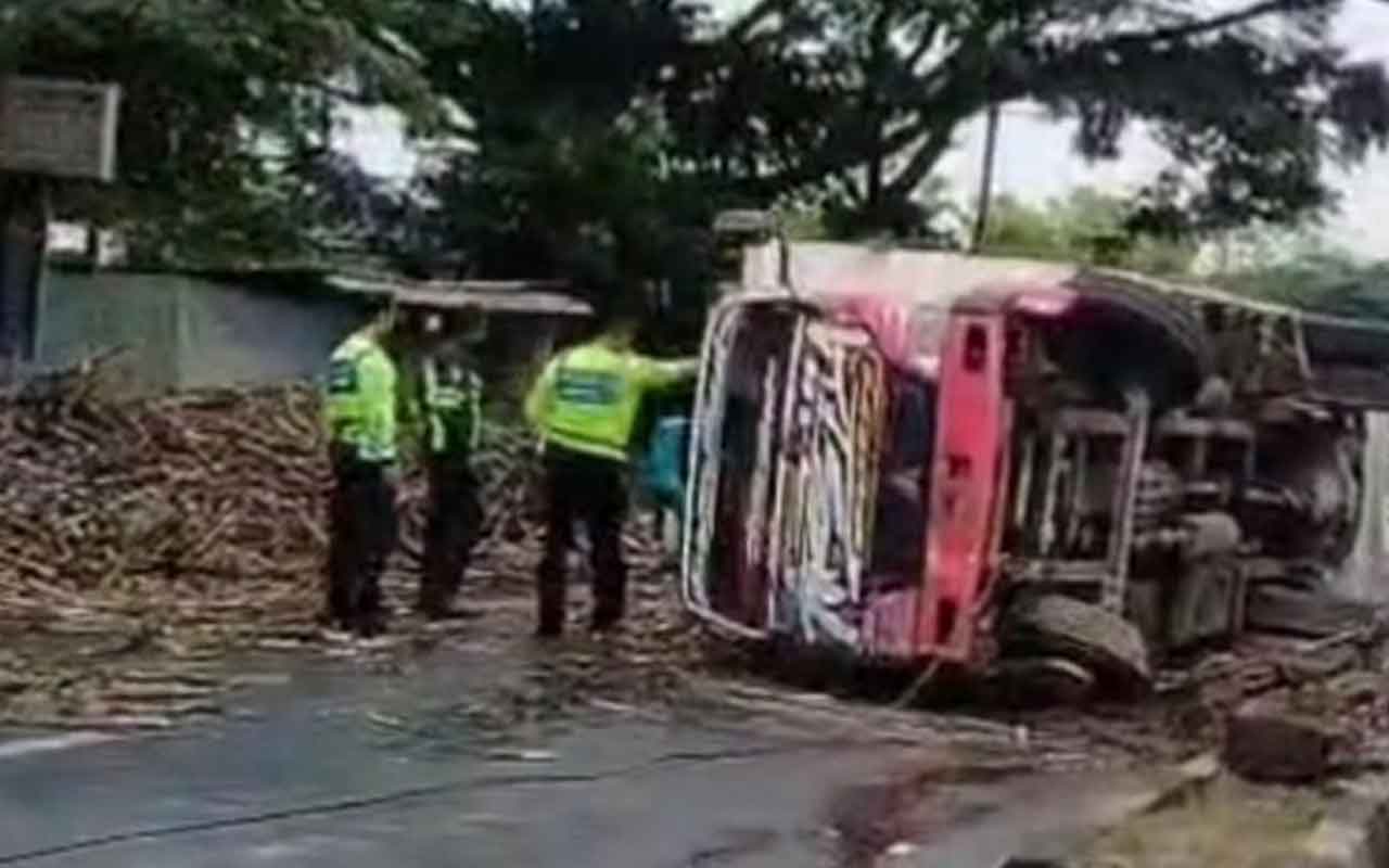 Pertugas saat membantu mengevakuasi truk dan muatan tebu yang berserakan di Jalan Purwosari, Pasuruan, Rabu (12/11/2025). 