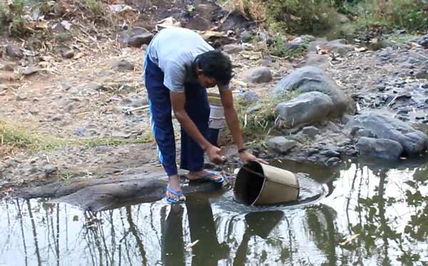 TERPAKSA: Seorang warga Desa Sambirobyong Kecamatan Berbek mengambil air sungai akibat sumur kering. foto: soewandito/BANGSAONLINE