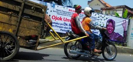 Pekerja kebersihan melintas di depan spanduk Walikota Surabaya, Tri Rismaharini. Spanduk serupa bertebaran di sejumlah tempat. (Maulana/BANGSAONLINE)