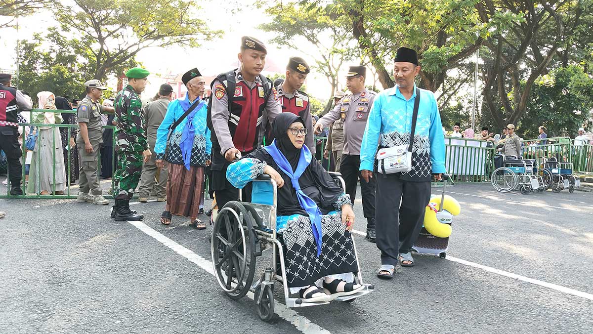 Salah satu calon jemaah haji dari Kabupaten Kediri saat dibantu petugas untuk menuju bus yang akan membawanya ke Surabaya. Foto: Ist