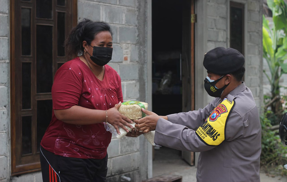 Bhabinkambtimas membagikan daging kurban secara door to door menggunakan besek.