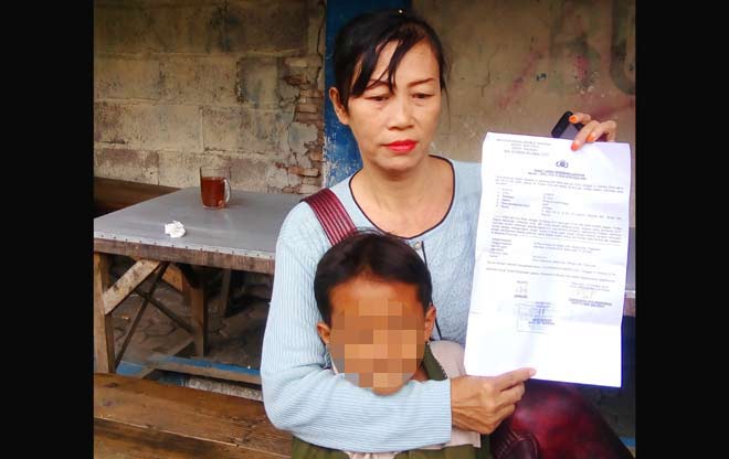 Juma’ati bersama anaknya, menunjukkan surat laporan ke polisi.