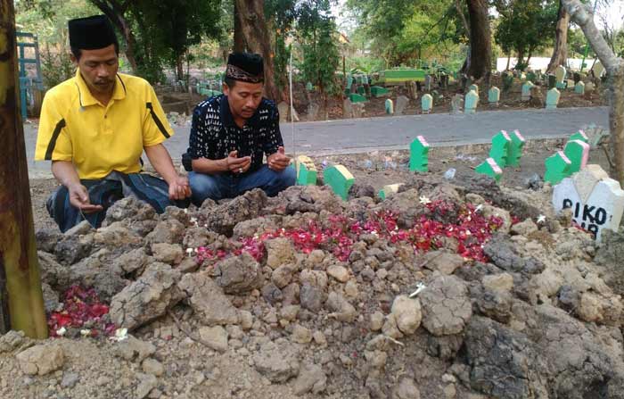 Keluarga berdoa di makan Riko, salah satu korban meninggal akibat pesta miras. foto: SYUHUD/ BANGSAONLINE