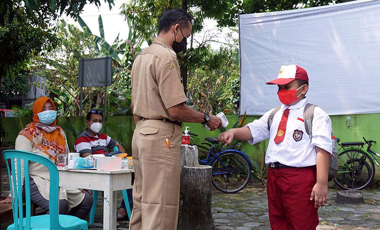 Seorang guru saat memeriksa suhu tubuh seorang siswa menggunakan thermogun. (foto: ist)