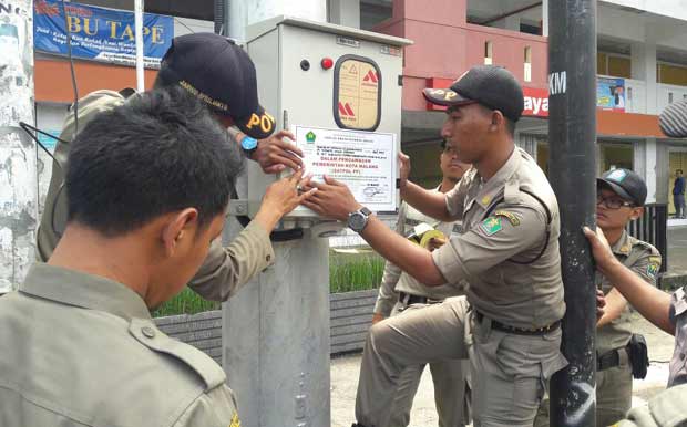 Petugas Satpol PP saat memasang stiker pelanggaran. foto: IWAN IRAWAN/ BANGSAONLINE