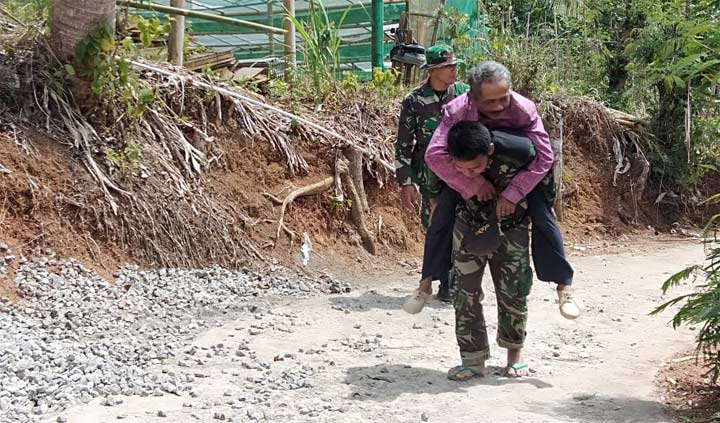 Prada Sugiarto dan Serka Tajib bahu membahu menggendong warga Desa Dompyong yang sakit.