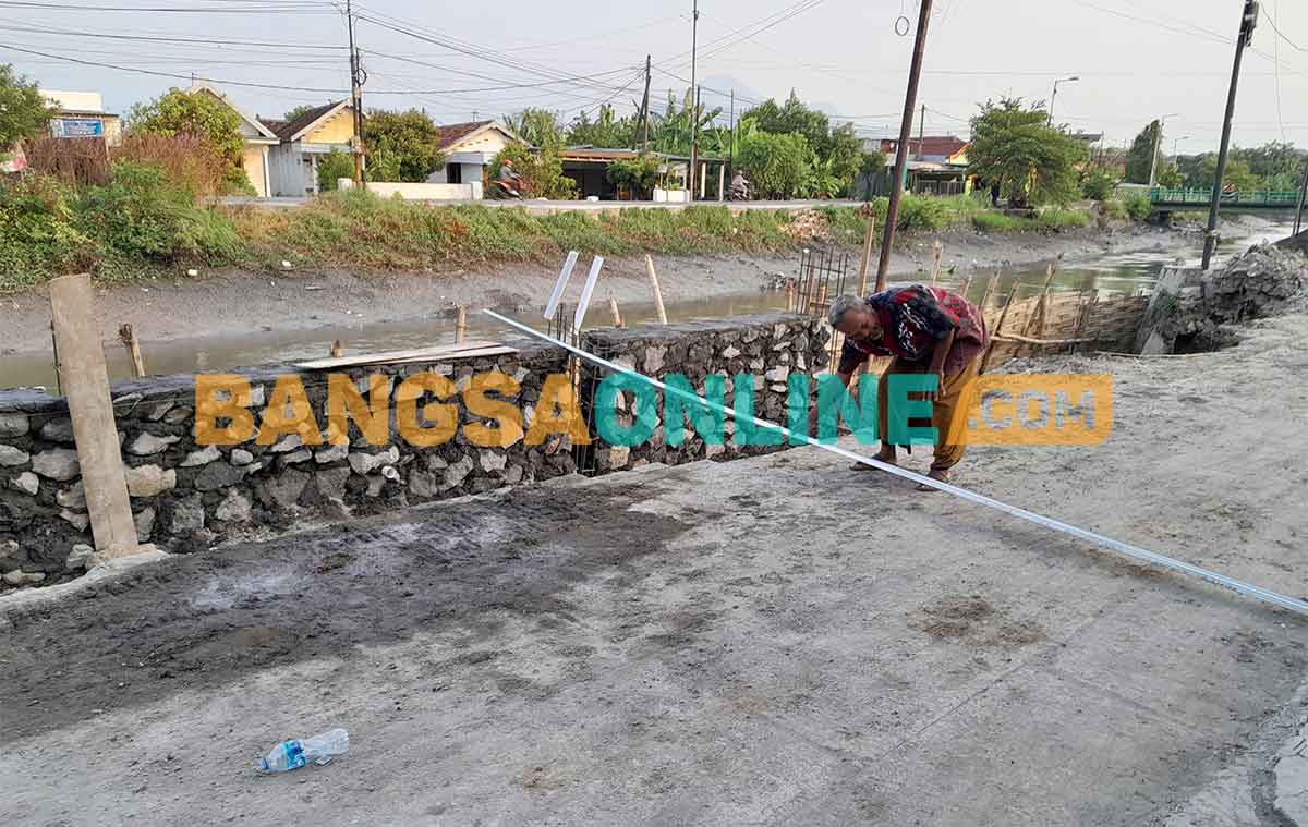 Warga mengukur jalan di samping proyek plengsengan di Desa Kemantren, Kecamatan Tulangan, Sidoarjo. Foto: MUSTAIN/BANGSAONLINE