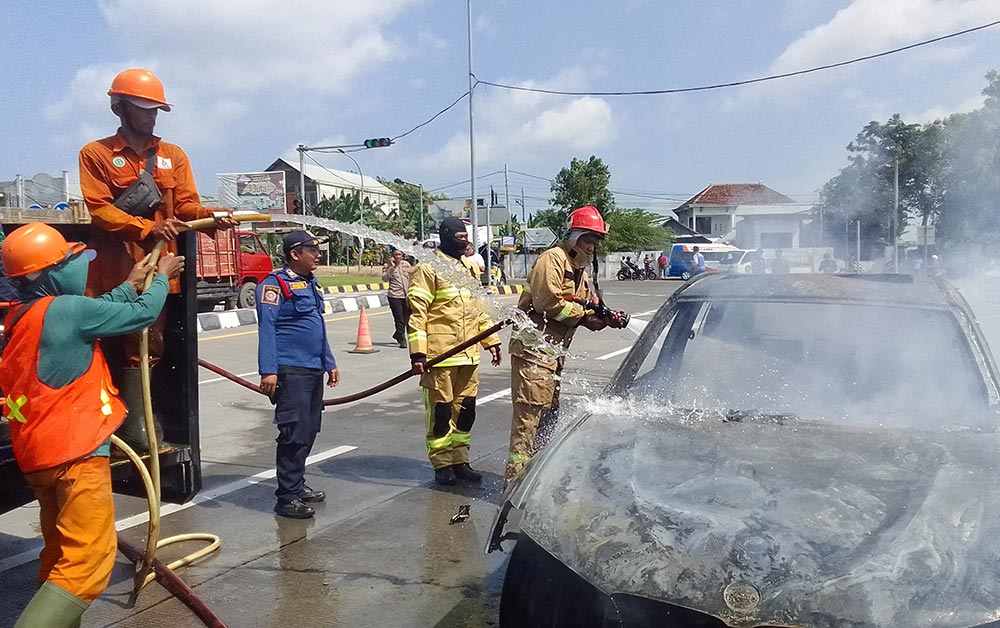 Petugas Damkar Gresik saat melakukan pembasahan pada mobil BMW yang terbakar di pintu masuk Tol Belahanrejo. Foto: Ist.