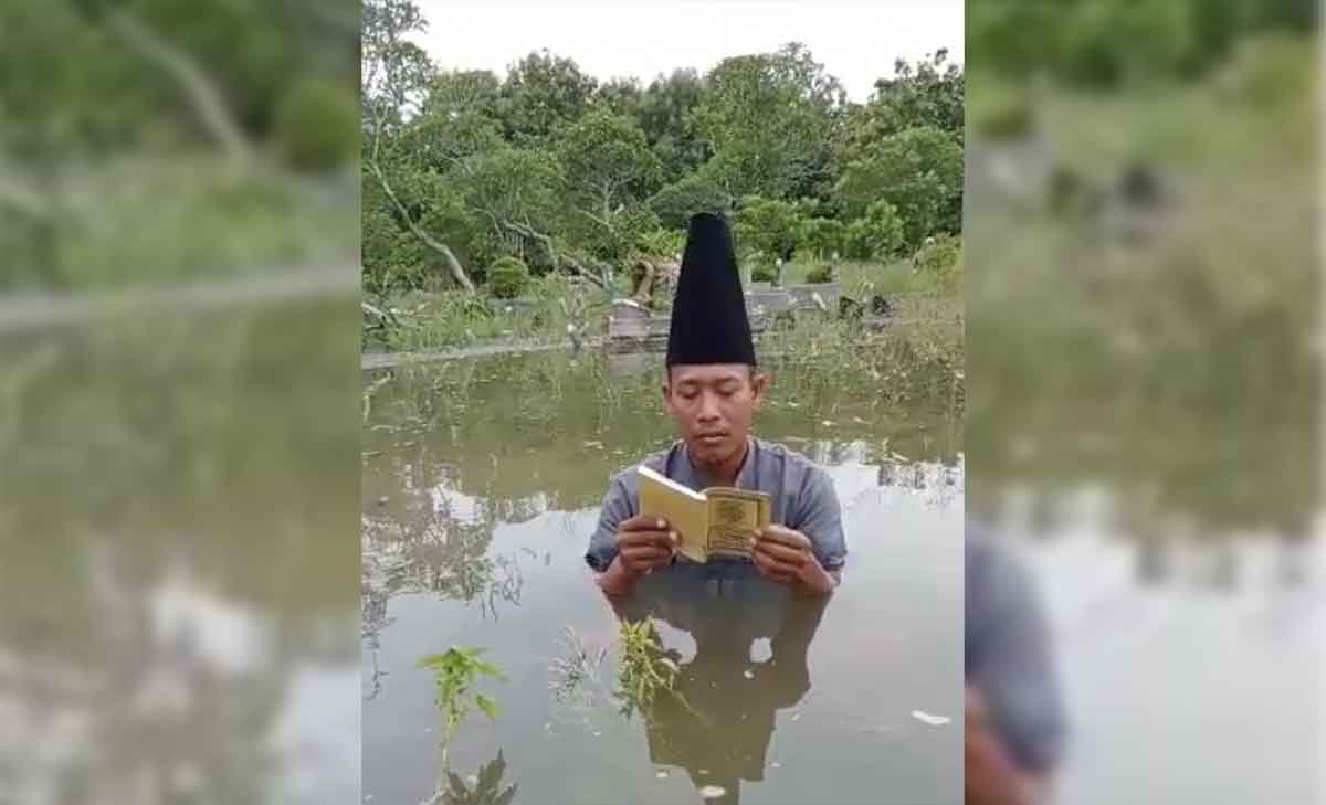 Hartono, warga Gading Watu, Kecamatan Menganti, Gresik, saat berdoa di makam yang terendam banjir. Foto: Ist
