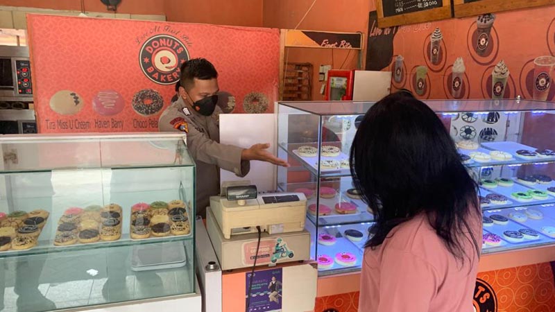 Anggota Bagops Polresta Sidoarjo, Bripka Dwi Agung Runsubekti, saat melayani pelanggan yang hendak membeli donat buatannya.