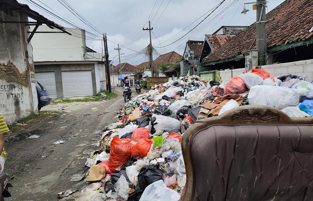 Pengendara motor melintas di Jalan Letnan Sunarto yang penuh gunungan sampah. Foto: Kompas.