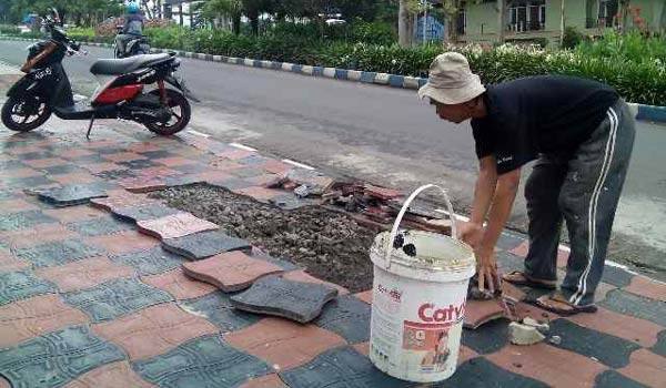 Warga yang khawatir memperbaiki sendiri trotoar yang rusak di depan rumah mereka.
